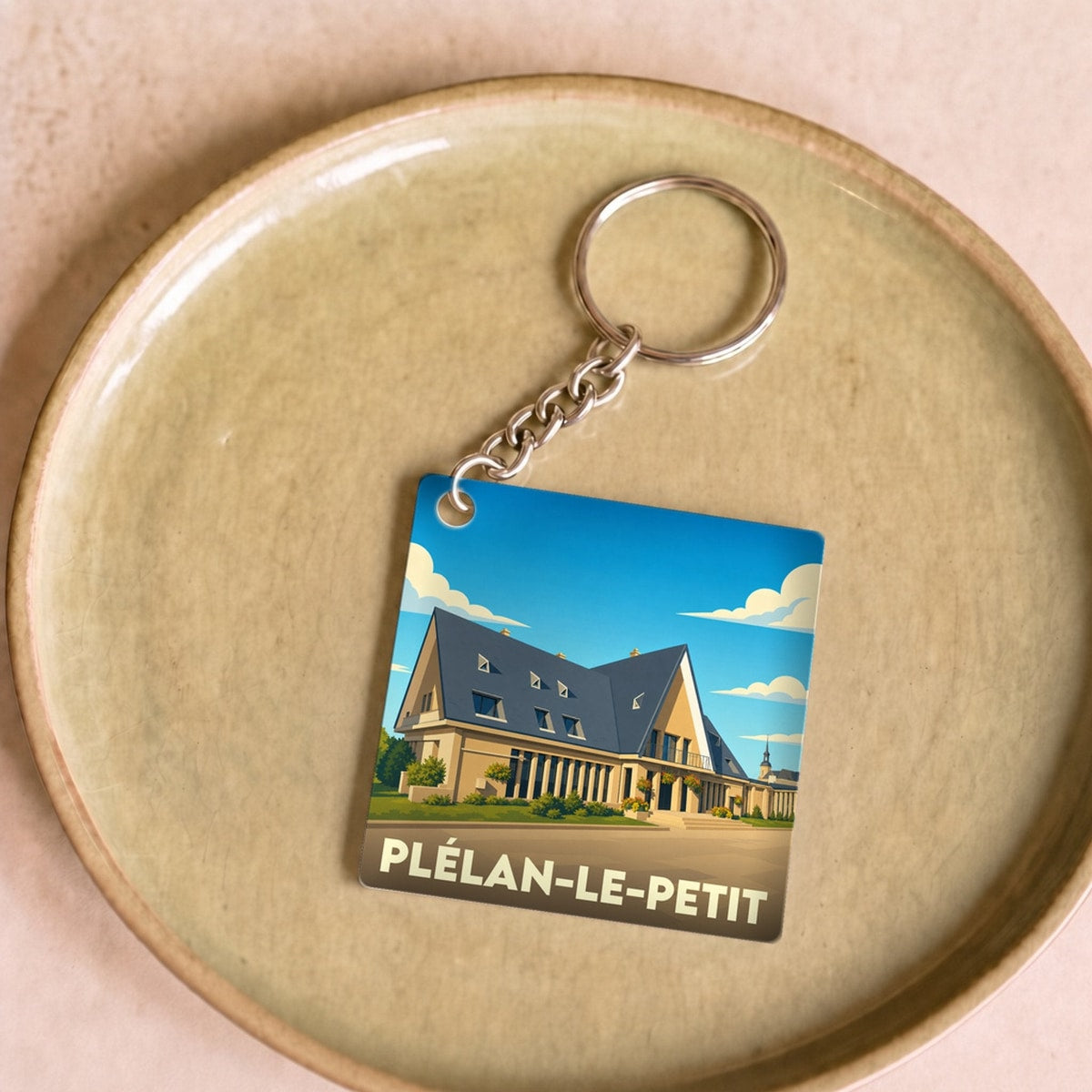 Porte-clés souvenir de la ville de Plélan-le-Petit avec une illustration stylisée.