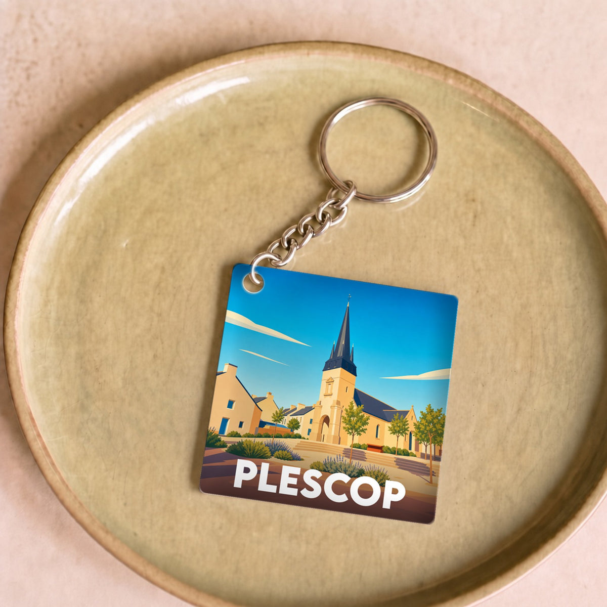 Porte-clés souvenir de la ville de Plescop avec une illustration stylisée d'une église sous un ciel bleu.