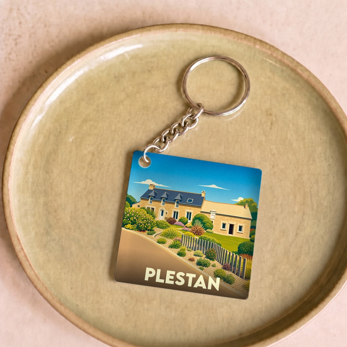 Porte-clés souvenir de la ville de Plestan avec une illustration stylisée d'une maison traditionnelle.
