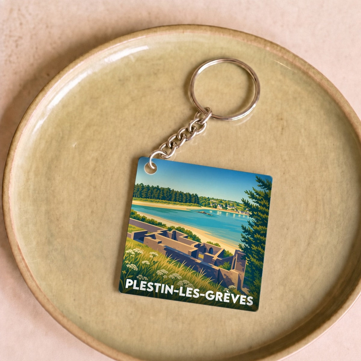Porte-clés souvenir de la ville de Plestin-les-Grèves avec une illustration stylisée de paysage côtier.