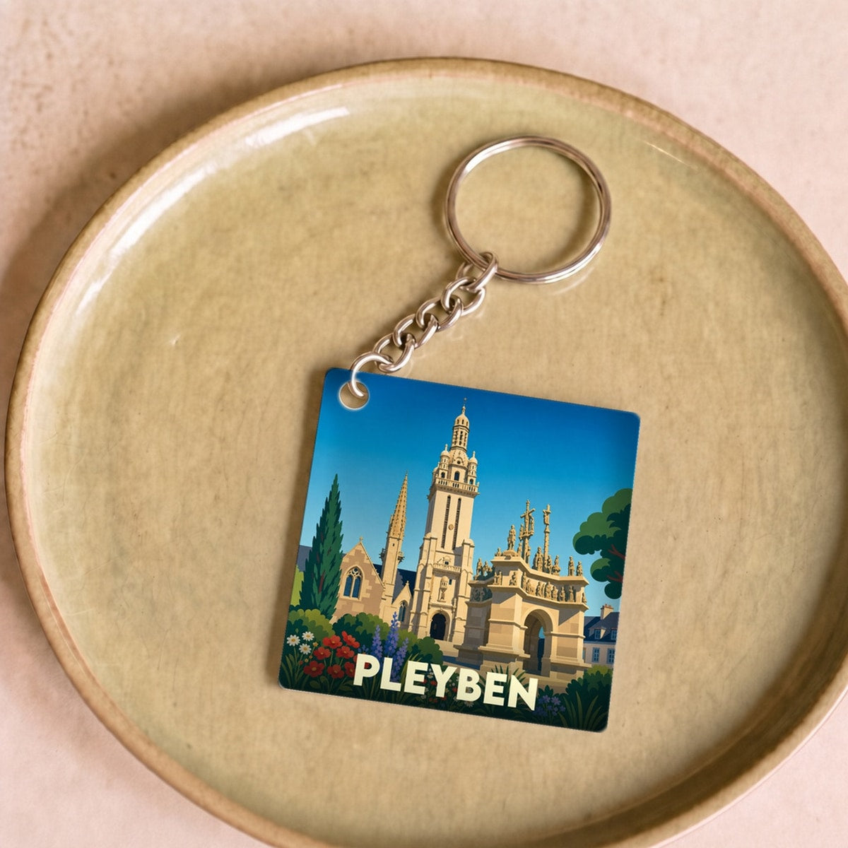 Porte-clés souvenir de la ville de Pleyben avec une illustration stylisée de son enclos paroissial.