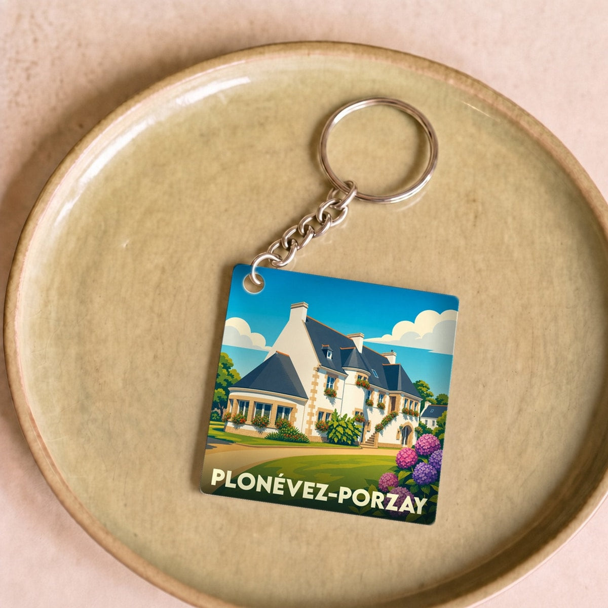 Porte-clés souvenir de la ville de Plonévez-Porzay avec une illustration stylisée d'une maison bretonne et d'hortensias.