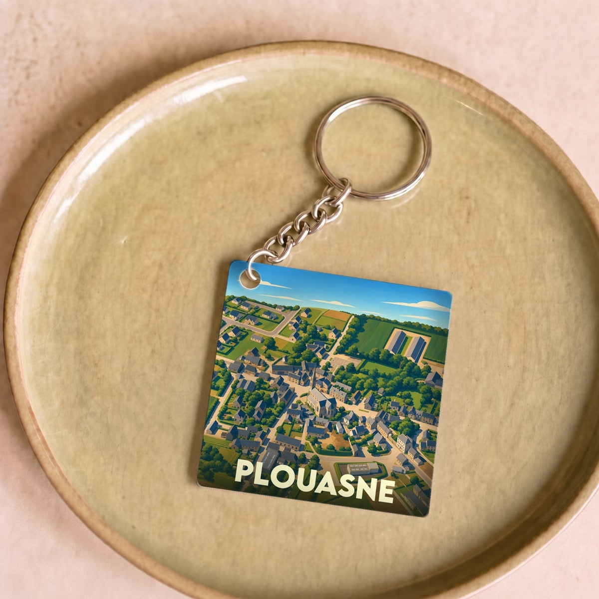 Porte-clés souvenir de la ville de Plouasne avec une illustration aérienne stylisée.