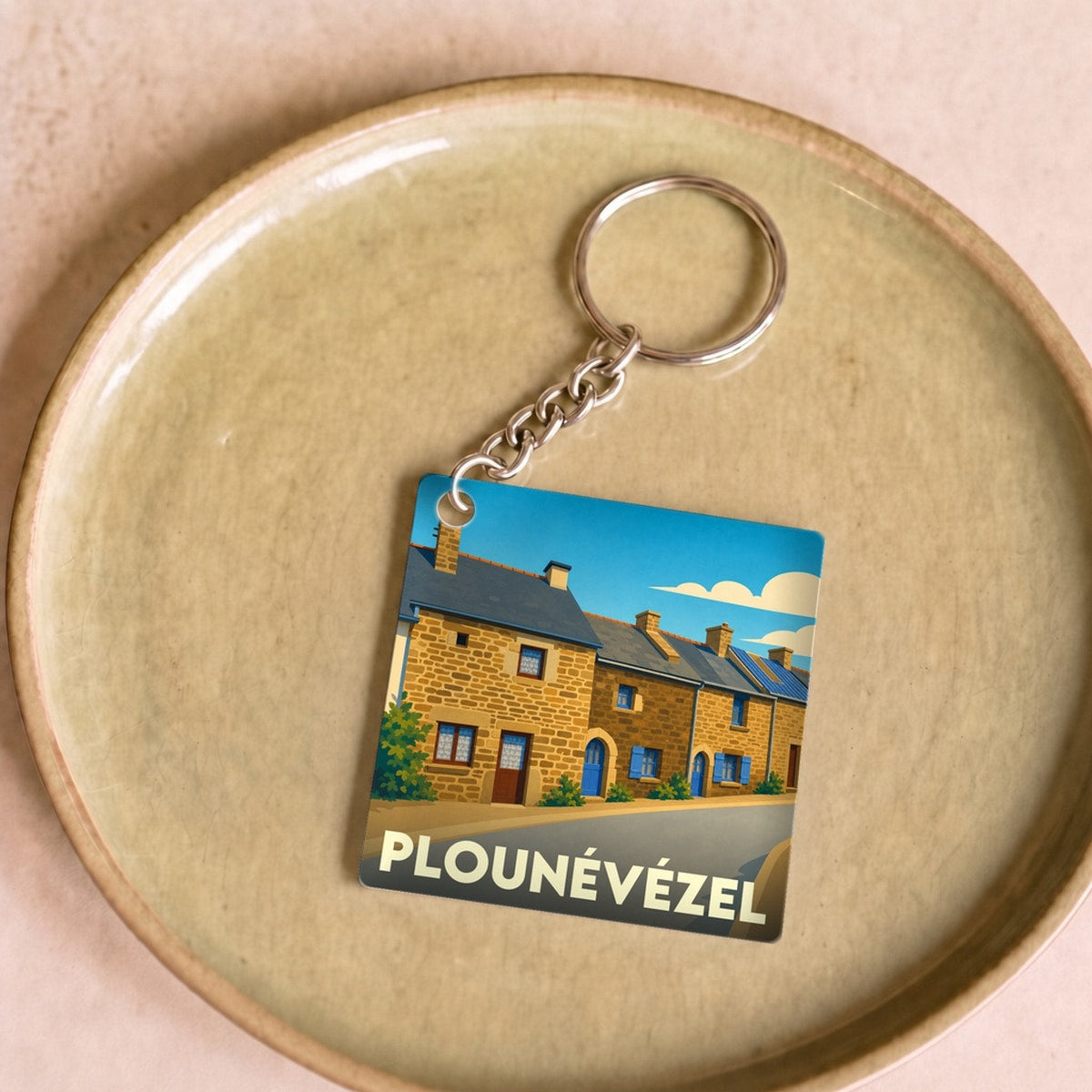 Porte-clés souvenir de la ville de Plounévézel avec une illustration stylisée de maisons traditionnelles.
