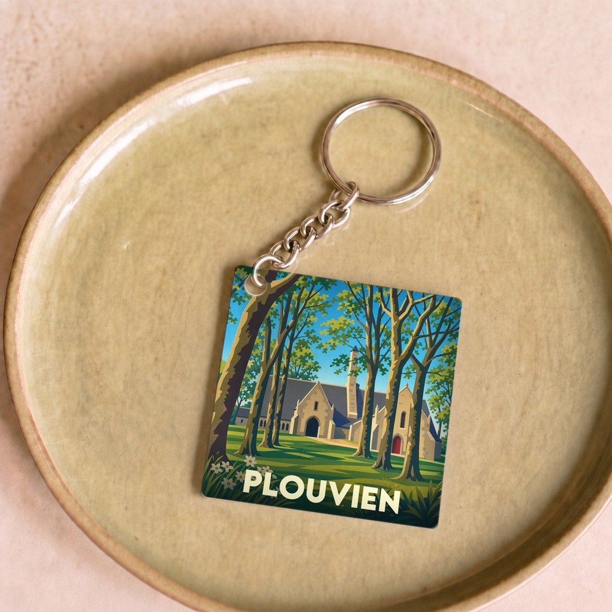 Porte-clés souvenir de la ville de Plouvien avec une illustration stylisée d'un monument historique entouré de forêt.