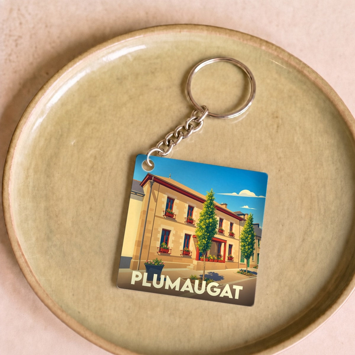 Porte-clés souvenir de la ville de Plumaugat avec une illustration stylisée d'un bâtiment fleuri.