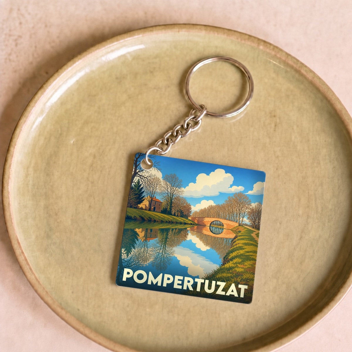 Porte-clés souvenir de la ville de Pompertuzat avec une illustration stylisée d'un paysage de canal.