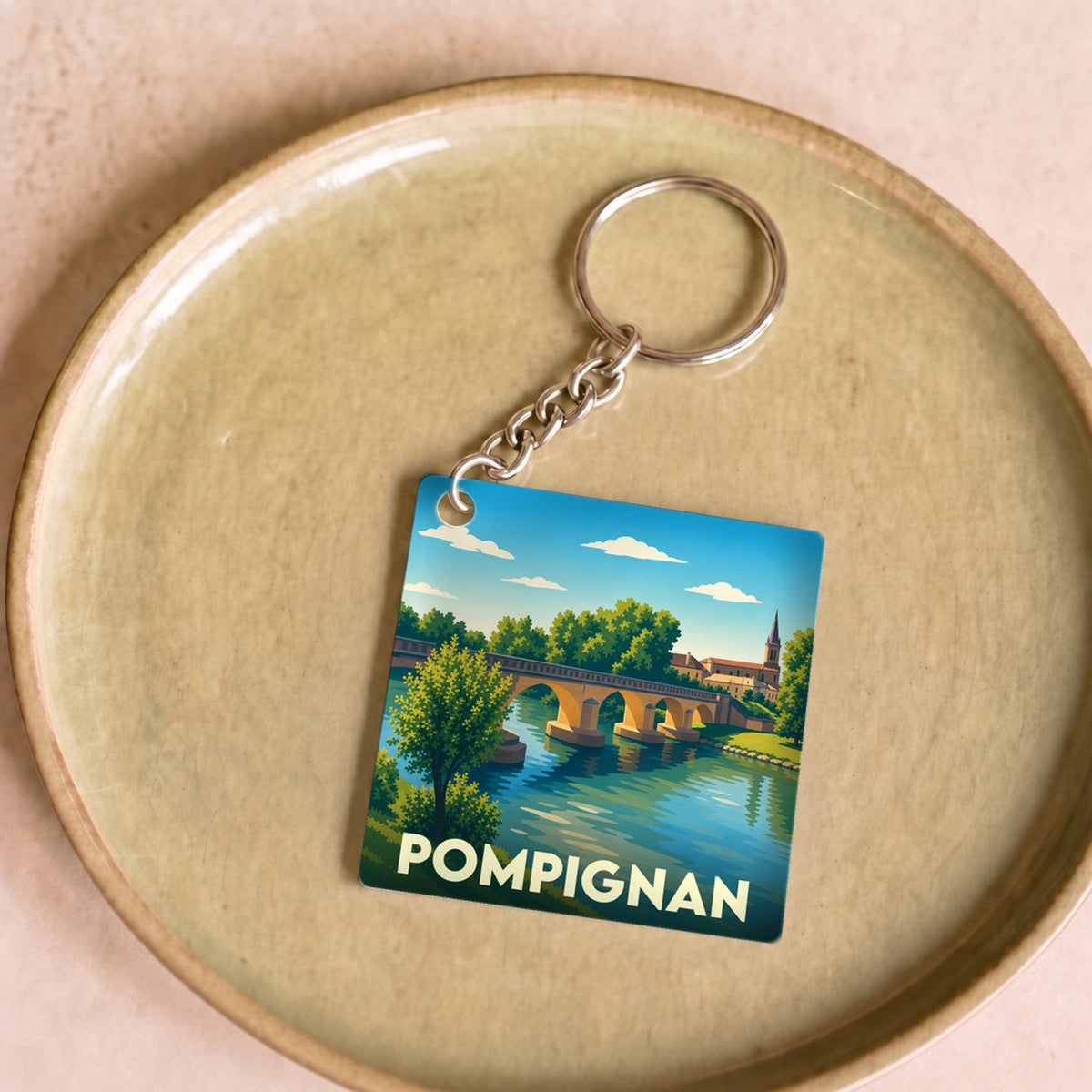 Porte-clés souvenir de la ville de Pompignan avec une illustration stylisée d'un pont sur une rivière.