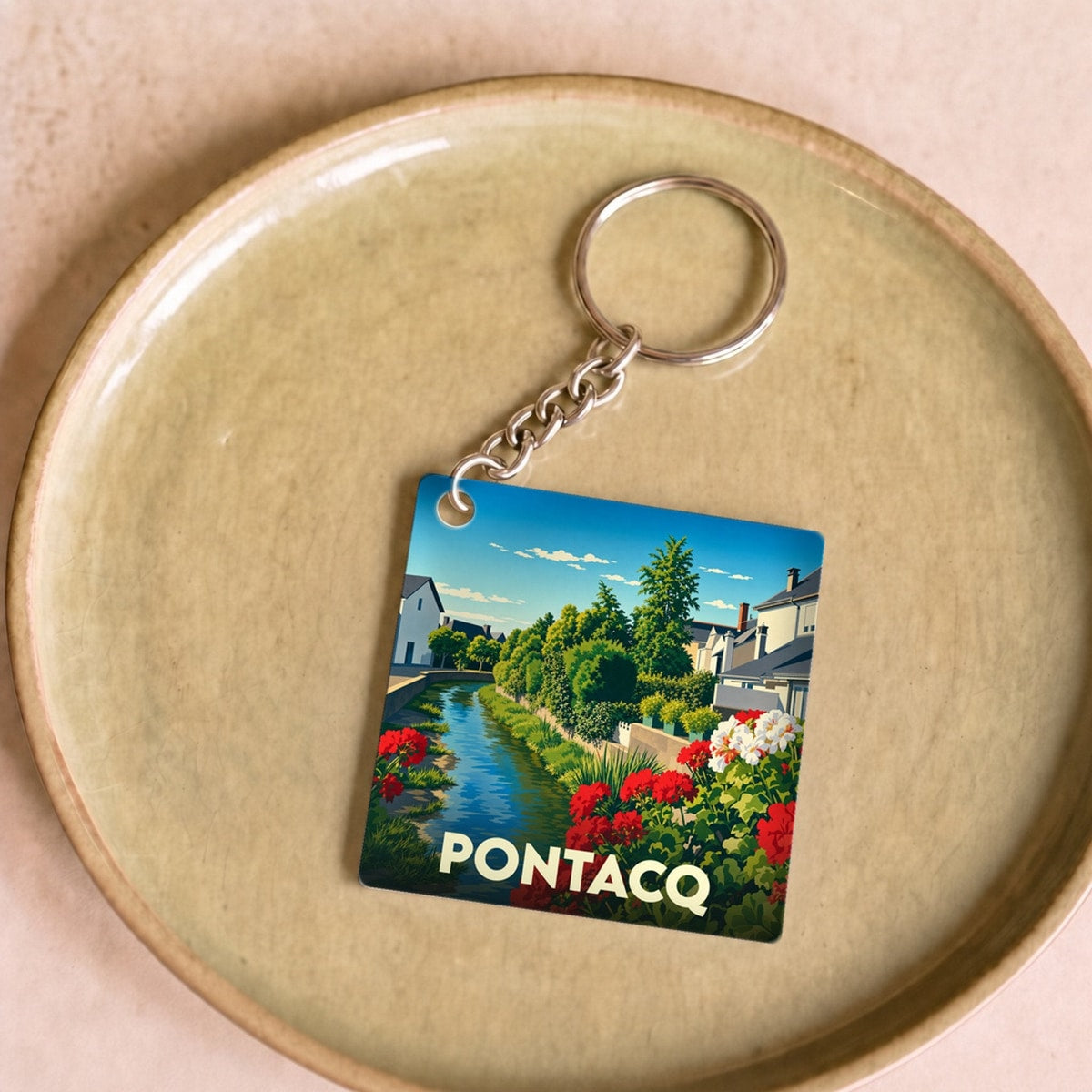Porte-clés souvenir de la ville de Pontacq avec une illustration stylisée d'un canal fleuri.