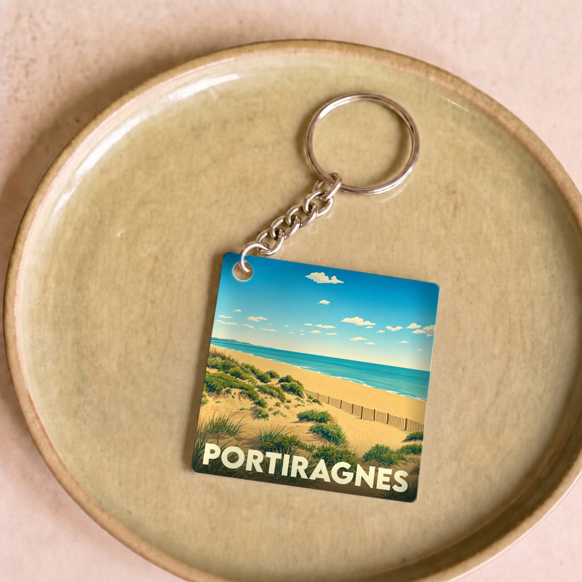 Porte-clés souvenir de la ville de Portiragnes avec une illustration stylisée de ses dunes et de la mer.