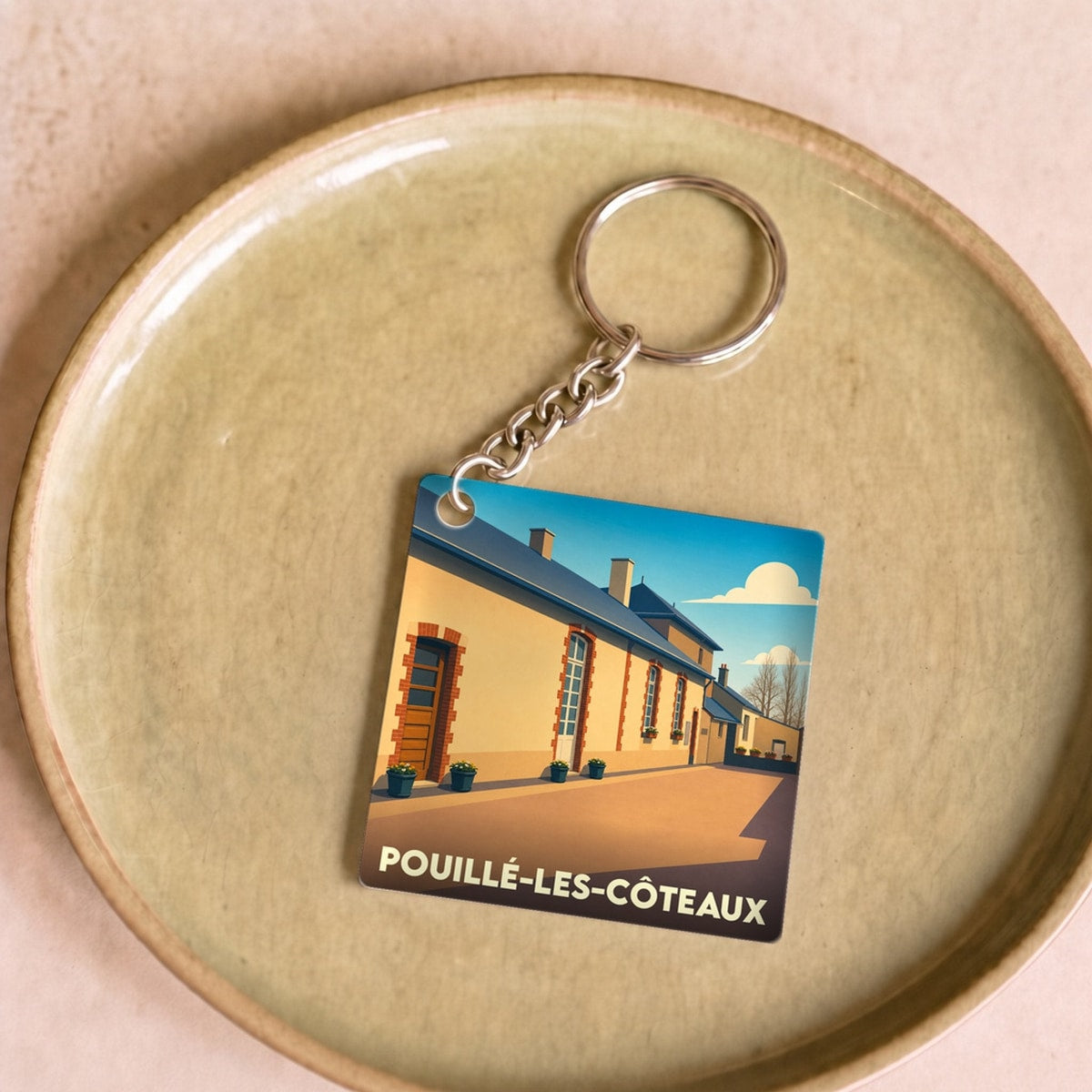 Porte-clés souvenir de la ville de Pouillé-les-Côteaux avec une illustration stylisée d'un bâtiment sous un ciel bleu.