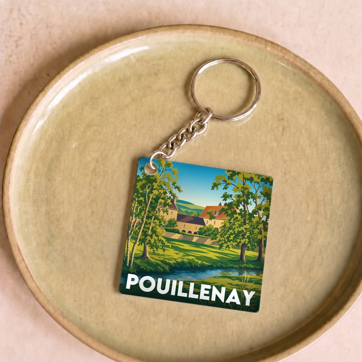 Porte-clés souvenir de la ville de Pouillenay avec une illustration paysagère stylisée.