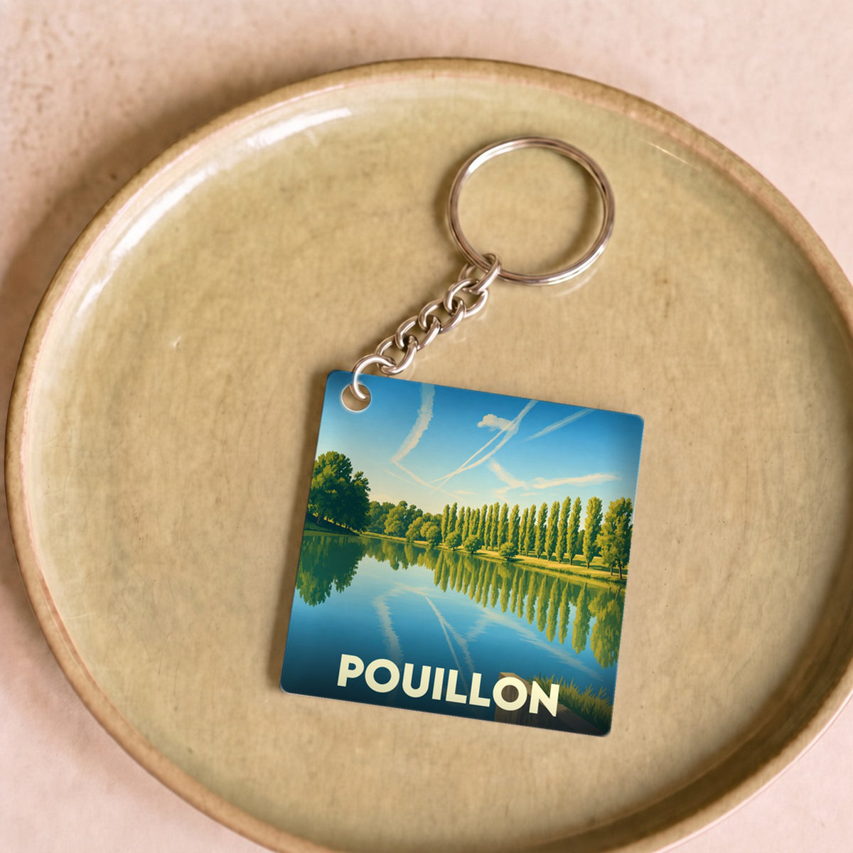 Porte-clés souvenir de la ville de Pouillon avec une illustration stylisée d'un lac bordé d'arbres.