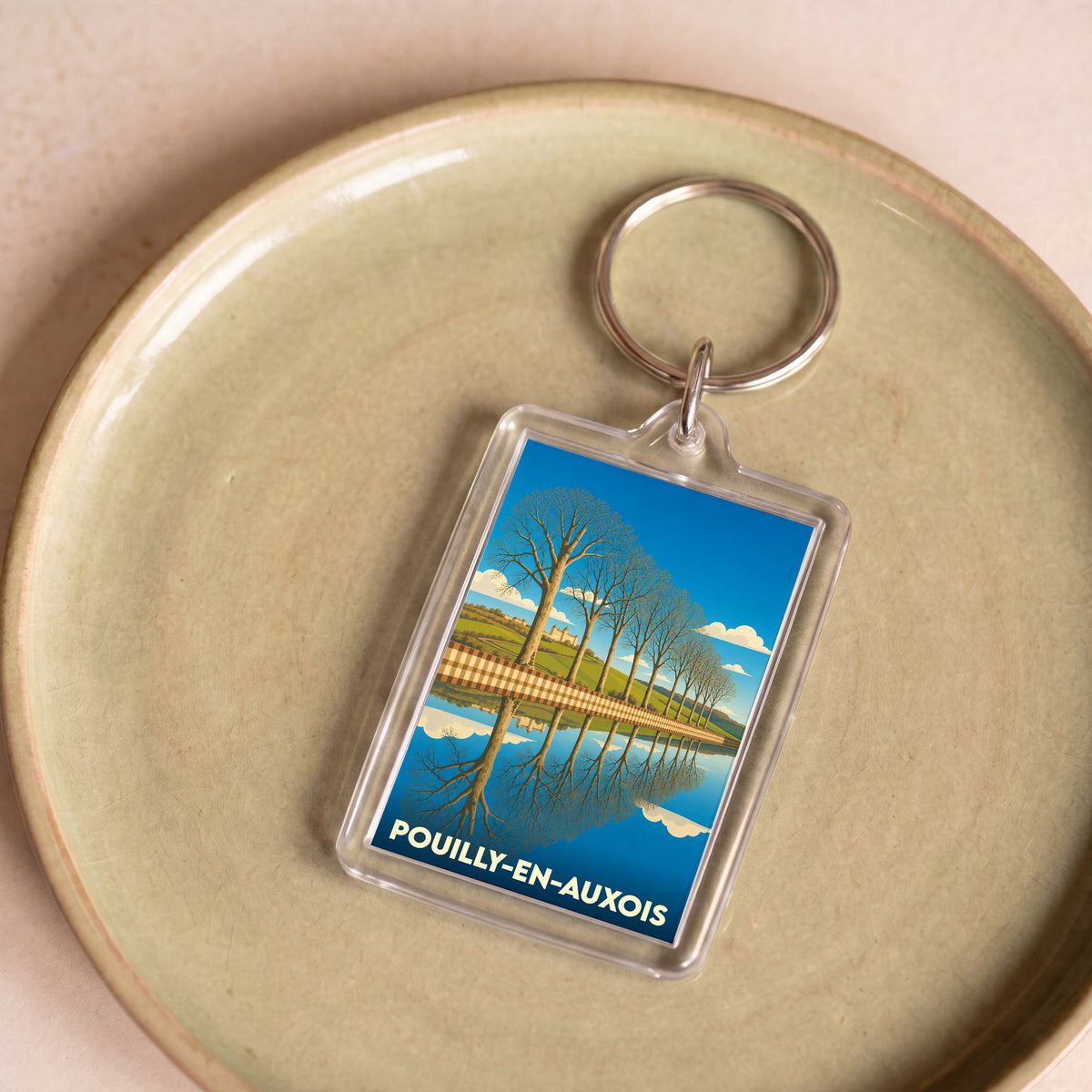 Porte-clés souvenir de Pouilly-en-Auxois illustrant une allée d'arbres se reflétant dans l'eau.
