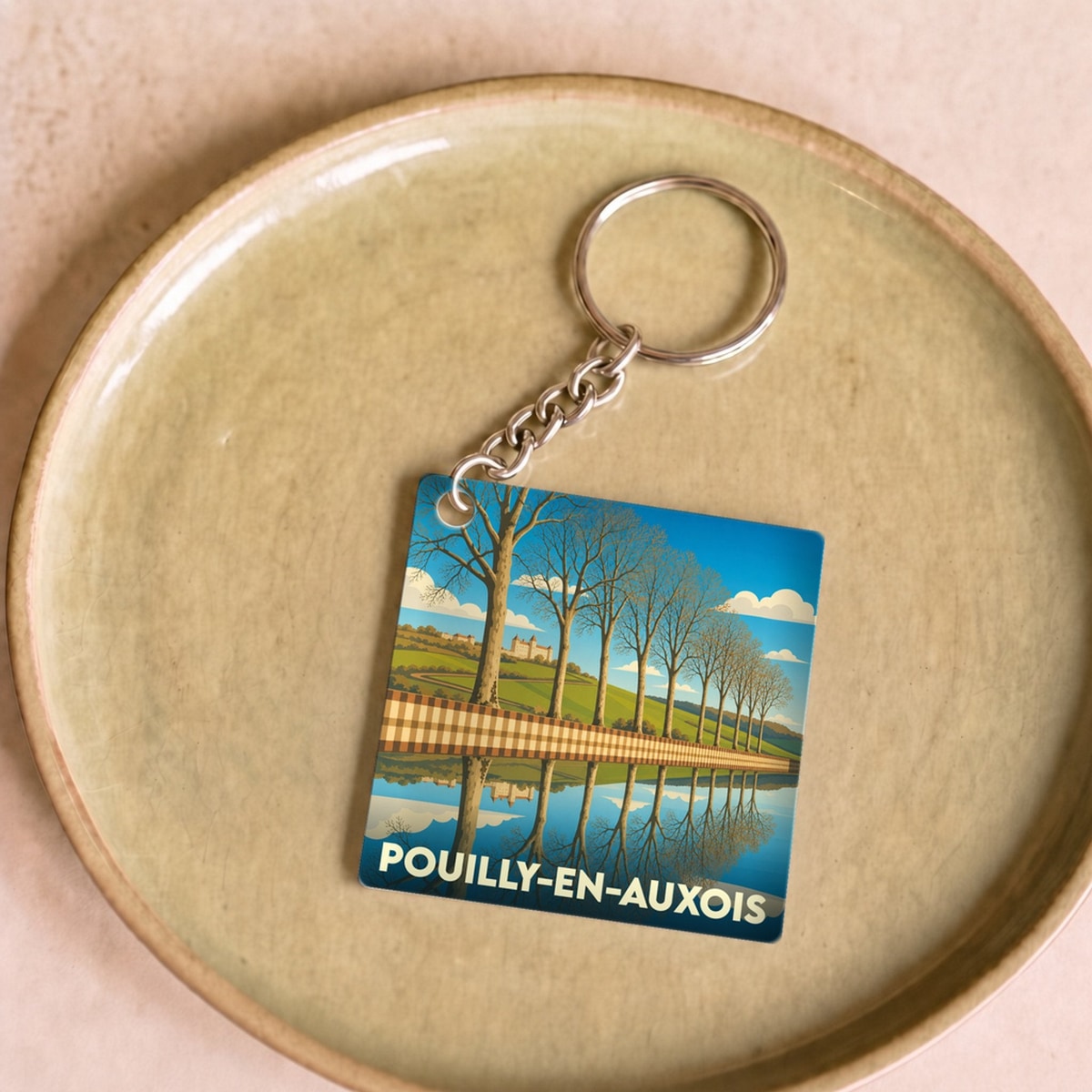 Porte-clés souvenir de Pouilly-en-Auxois illustrant une allée d'arbres se reflétant dans l'eau.