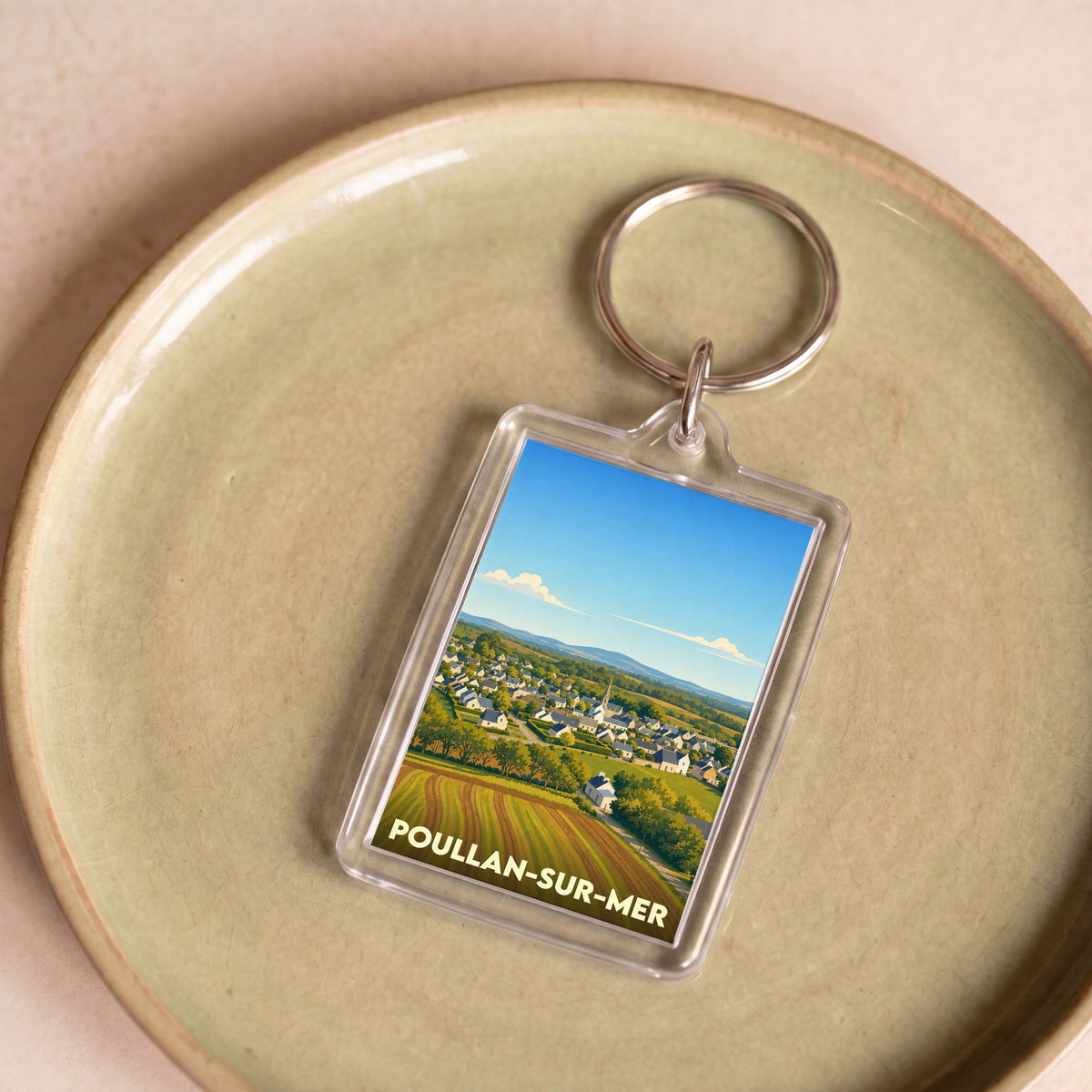 Porte-clés souvenir de la ville de Poullan-sur-Mer avec une illustration stylisée d'un paysage de campagne breton.