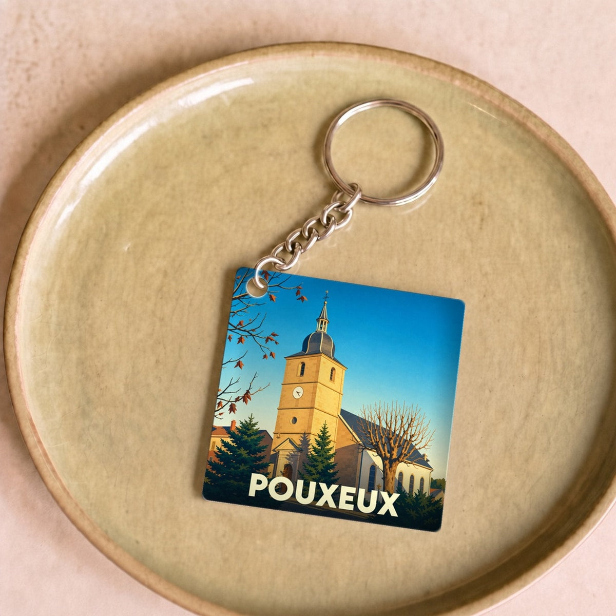 Porte-clés souvenir de la ville de Pouxeux avec une illustration stylisée de son église.