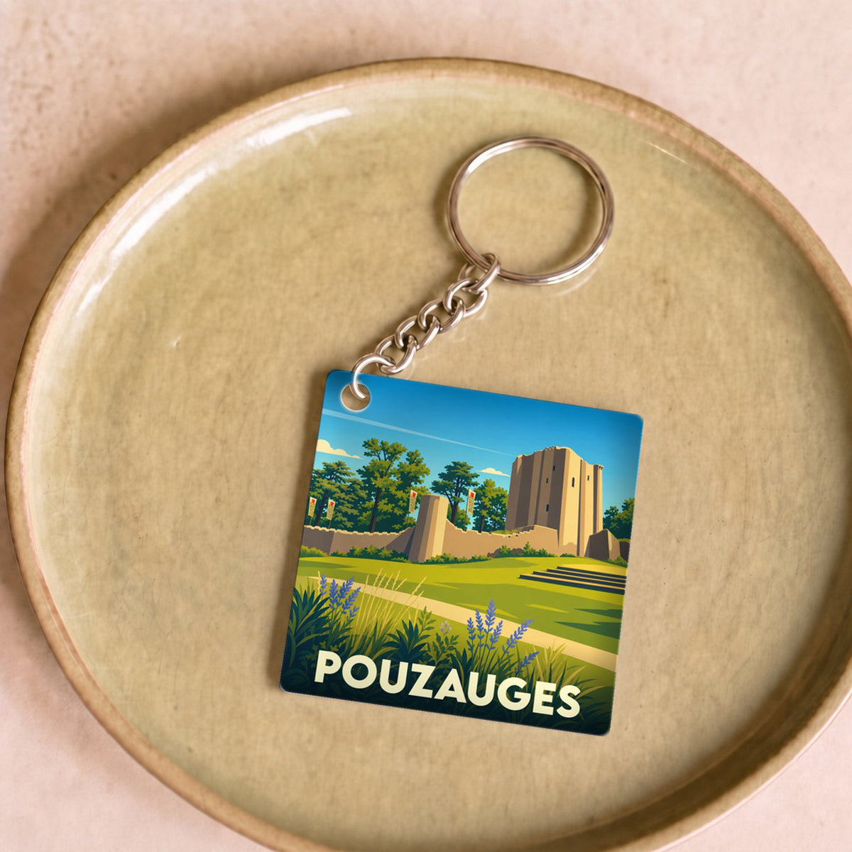 Porte-clés souvenir de la ville de Pouzauges avec une illustration stylisée de son château médiéval.