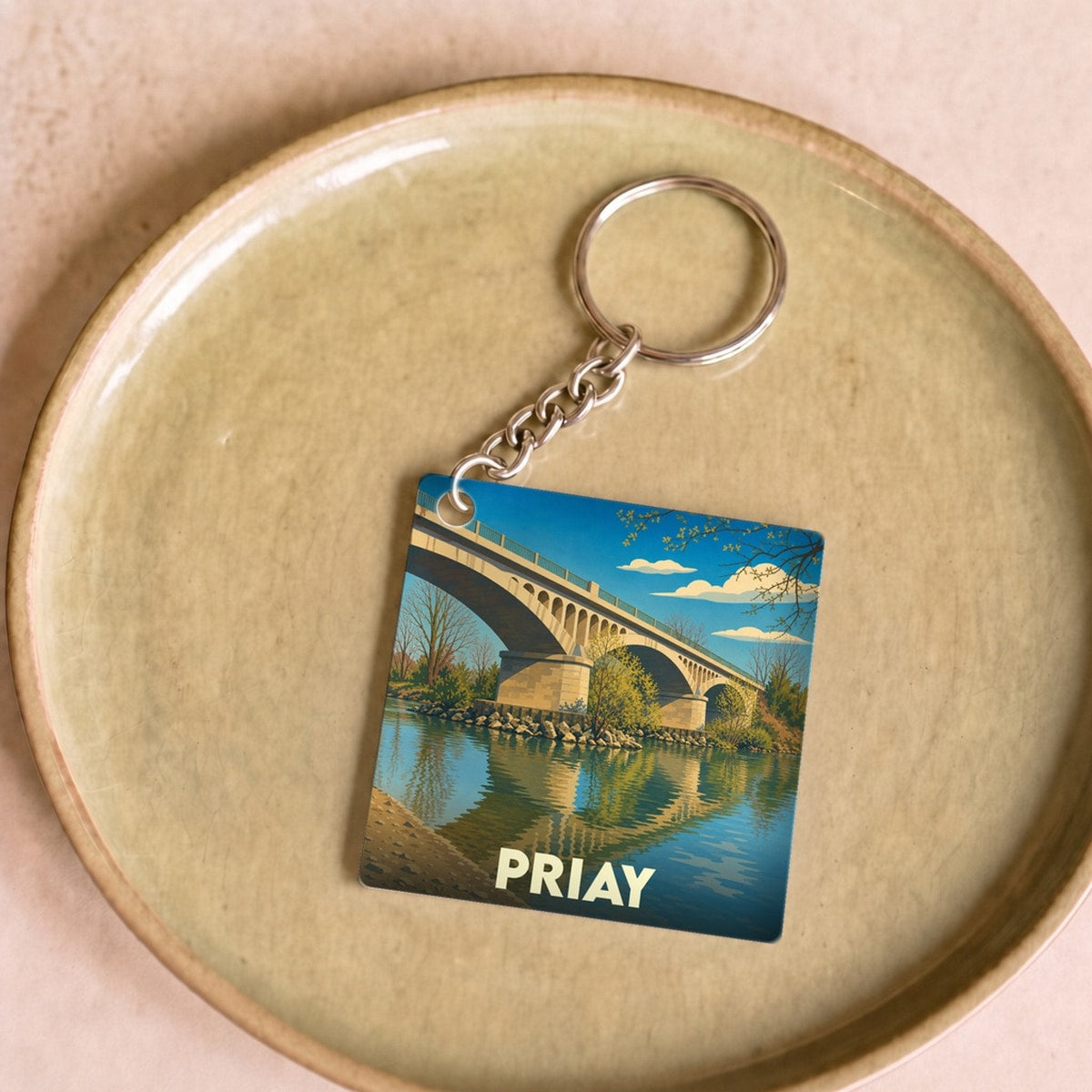 Porte-clés souvenir de la ville de Priay avec une illustration stylisée d'un pont se reflétant dans l'eau.