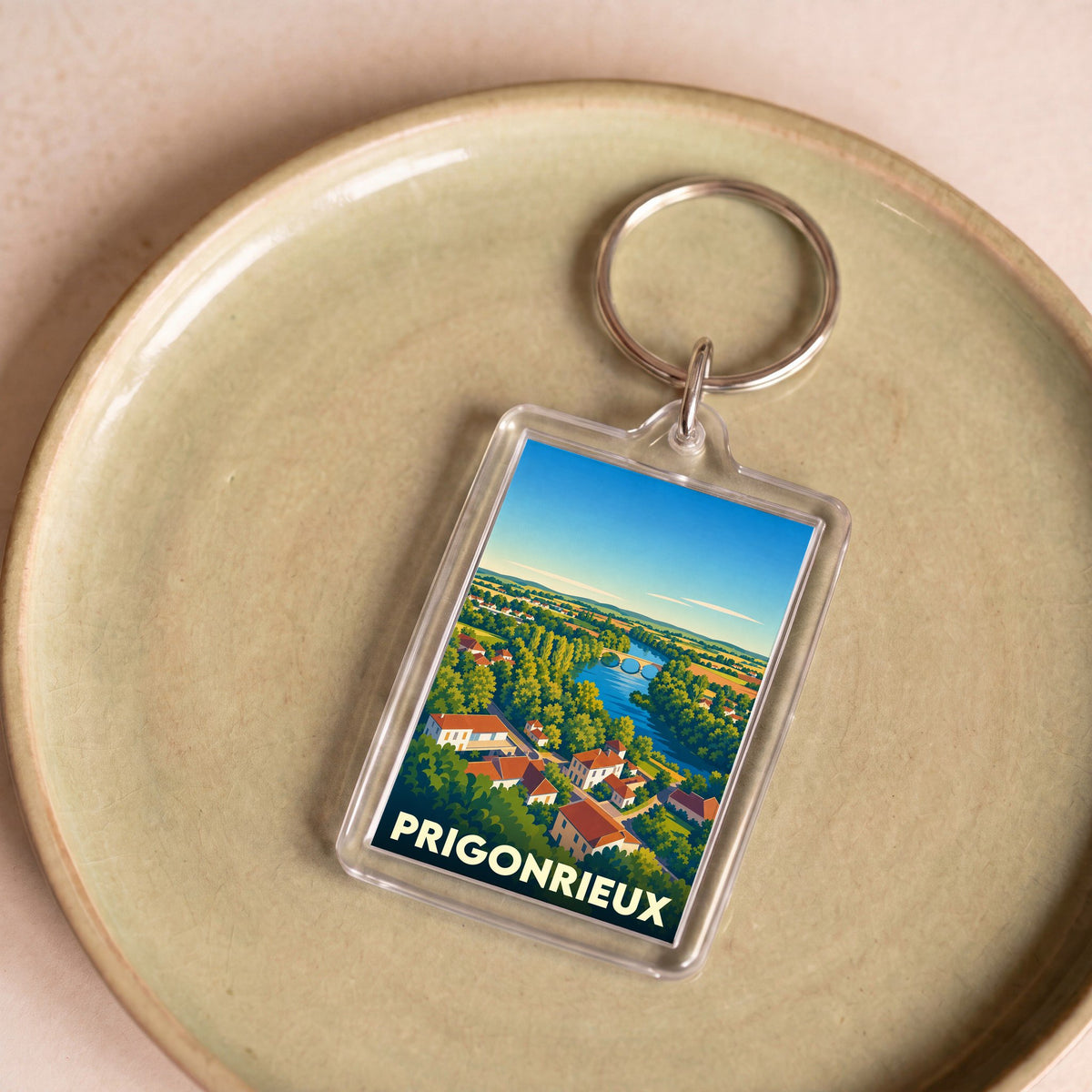 Porte-clés souvenir de la ville de Prigonrieux avec une illustration stylisée d'un paysage fluvial.