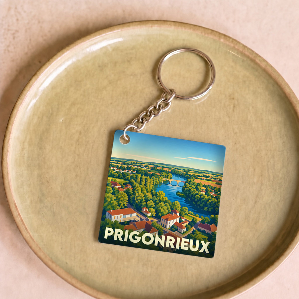 Porte-clés souvenir de la ville de Prigonrieux avec une illustration stylisée d'un paysage fluvial.