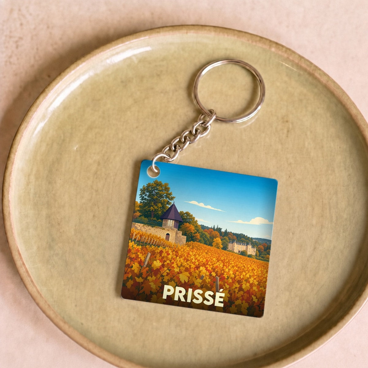 Porte-clés souvenir de la ville de Prissé avec une illustration stylisée de vignobles en automne.
