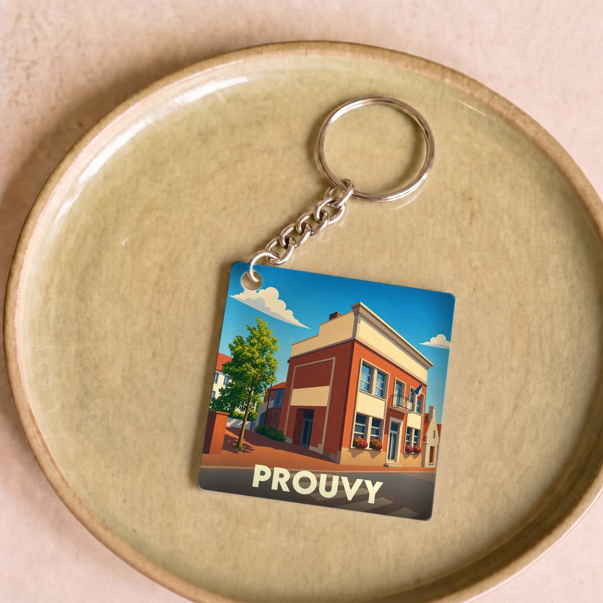 Porte-clés souvenir de la ville de Prouvy avec une illustration stylisée d'un bâtiment urbain sous un ciel bleu.