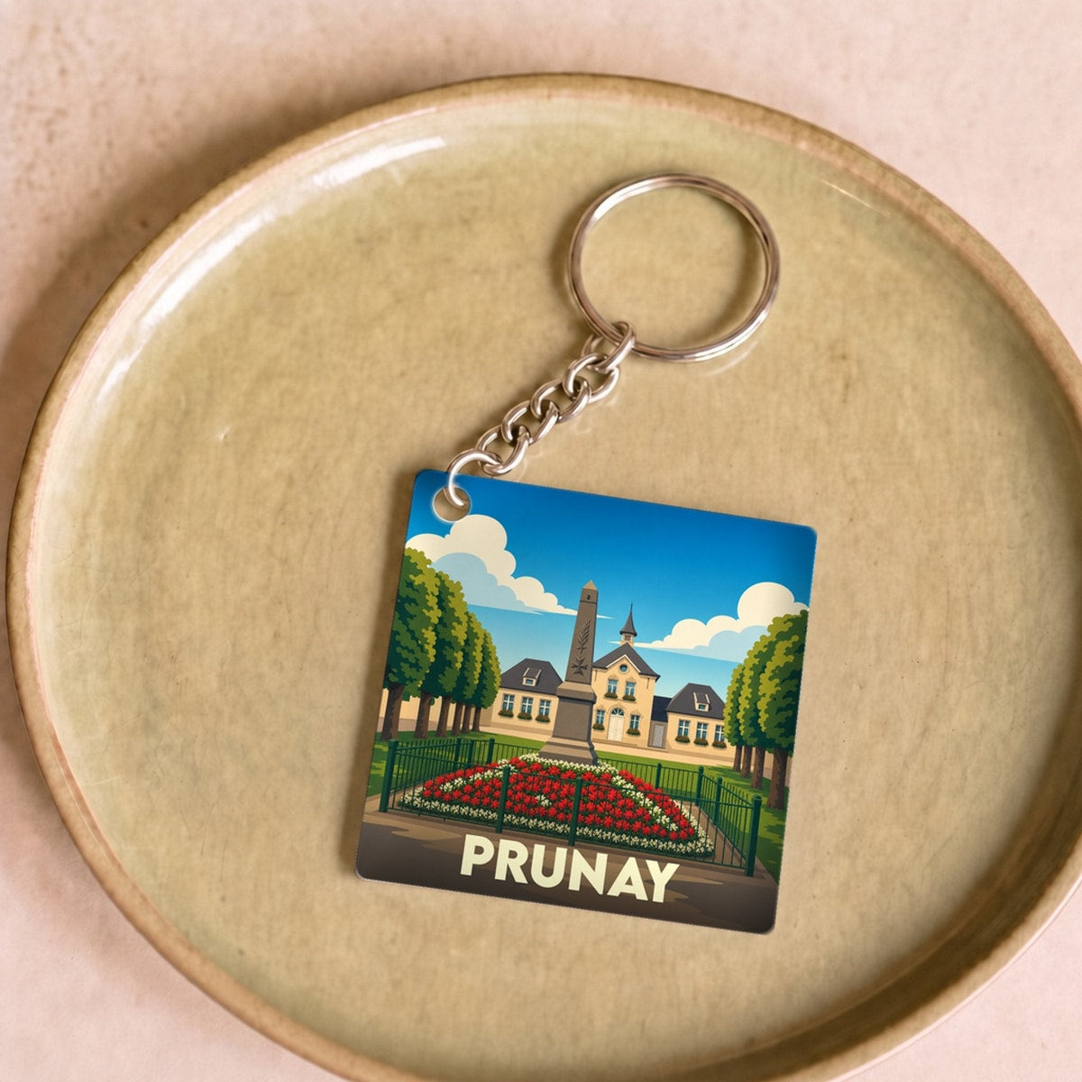 Porte-clés souvenir de la ville de Prunay avec une illustration stylisée de son monument aux morts et de sa mairie.
