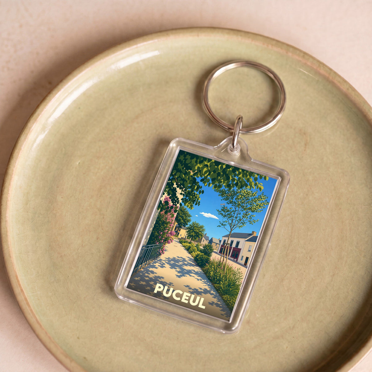 Porte-clés souvenir de la ville de Puceul avec une illustration stylisée d'une rue ensoleillée.