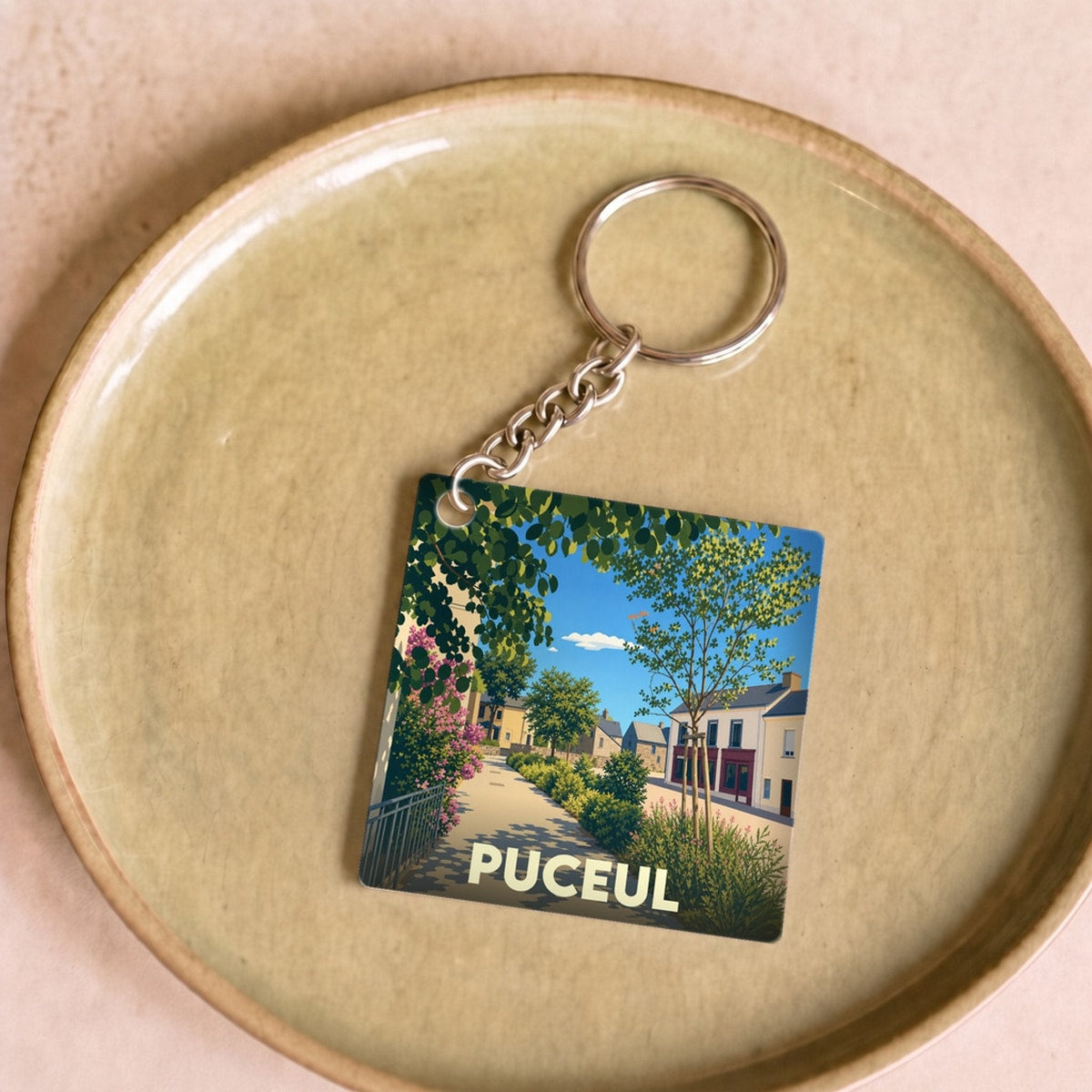 Porte-clés souvenir de la ville de Puceul avec une illustration stylisée d'une rue ensoleillée.