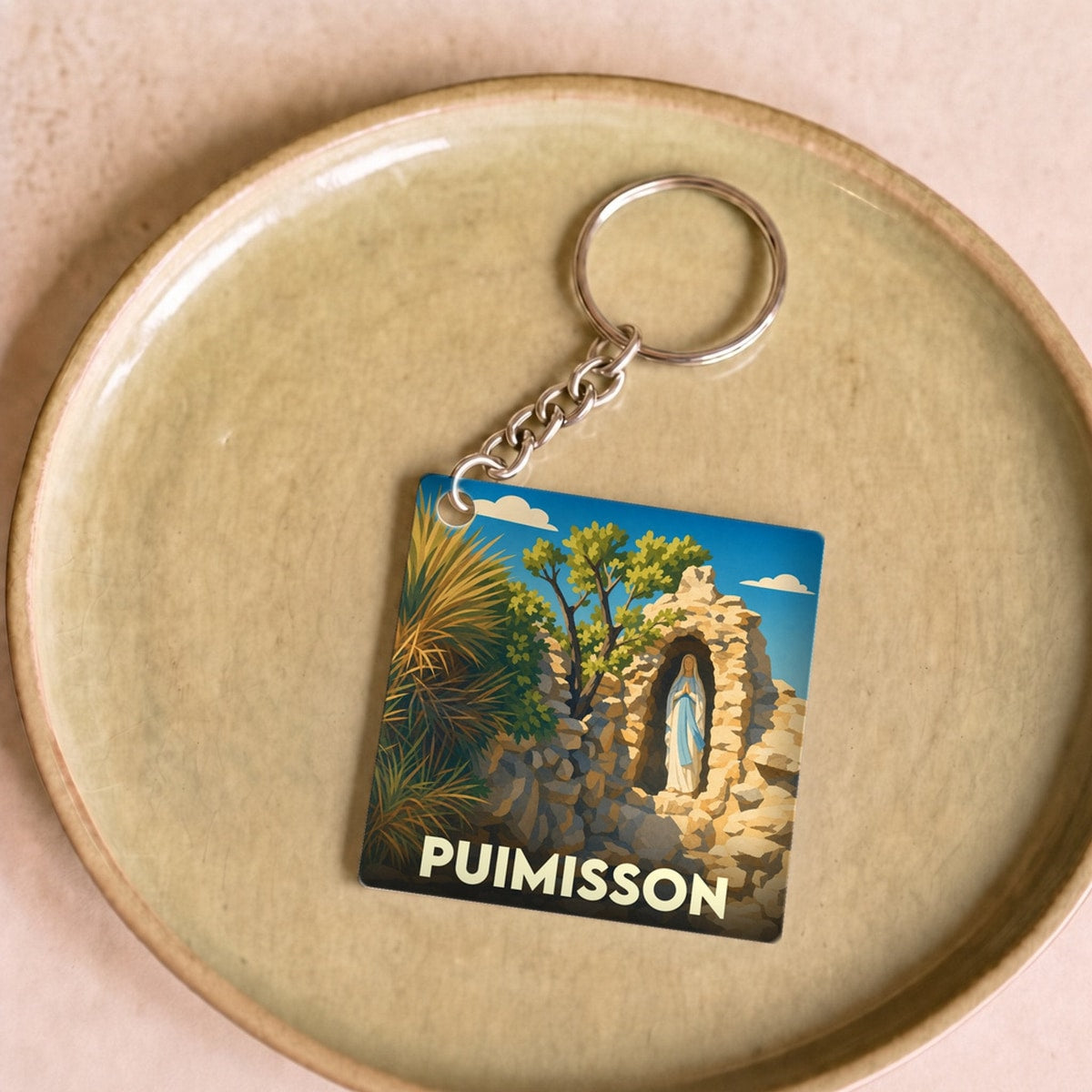 Porte-clés souvenir de la ville de Puimisson avec une illustration stylisée d'une statue dans une grotte de pierre.