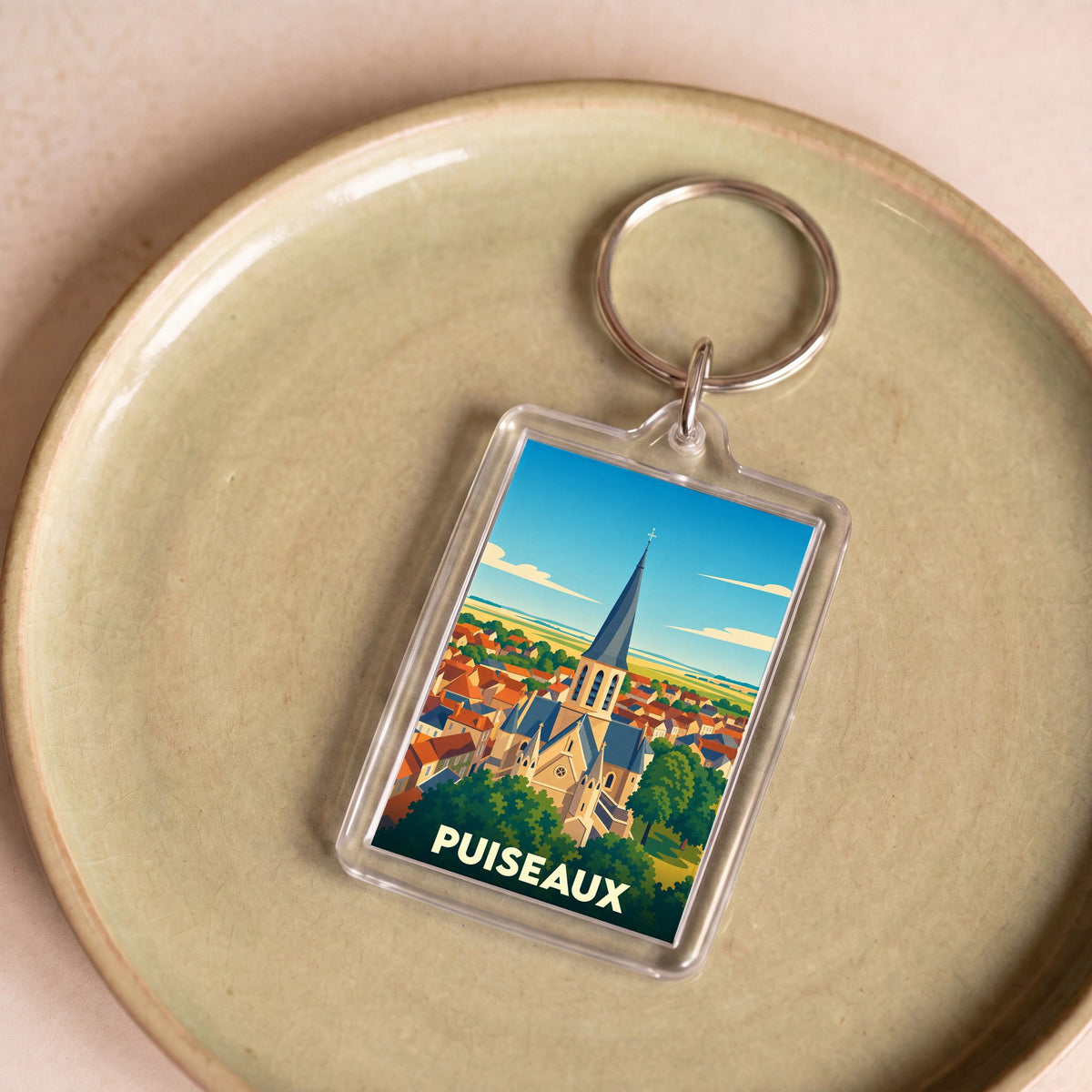 Porte-clés souvenir de la ville de Puiseaux avec une illustration stylisée de son église et de ses toits.
