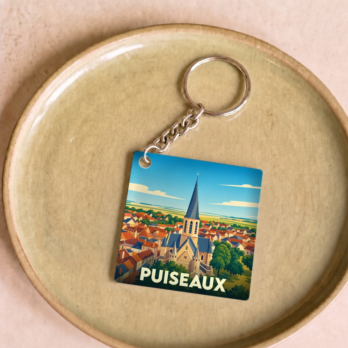 Porte-clés souvenir de la ville de Puiseaux avec une illustration stylisée de son église et de ses toits.