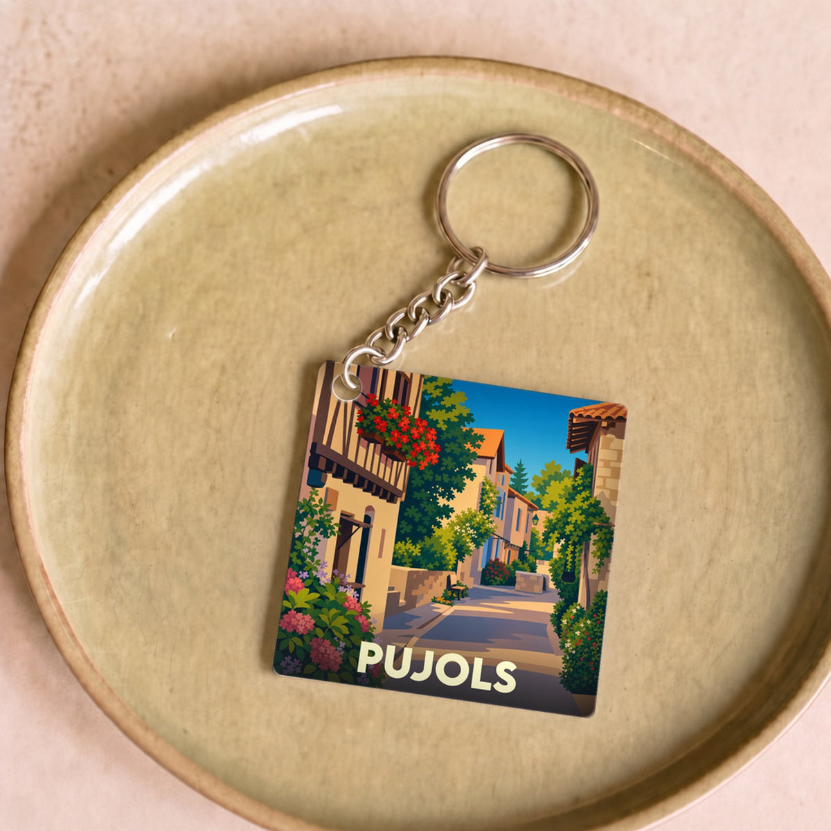 Porte-clés souvenir de la ville de Pujols avec une illustration stylisée d'une ruelle fleurie.