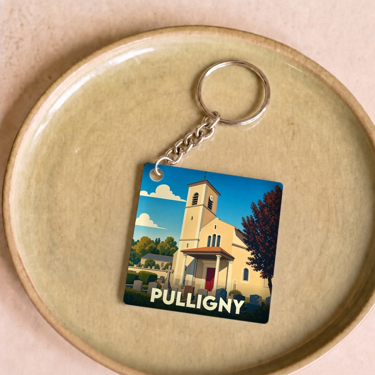 Porte-clés souvenir de la ville de Pulligny avec une illustration stylisée d'une église sous un ciel bleu.