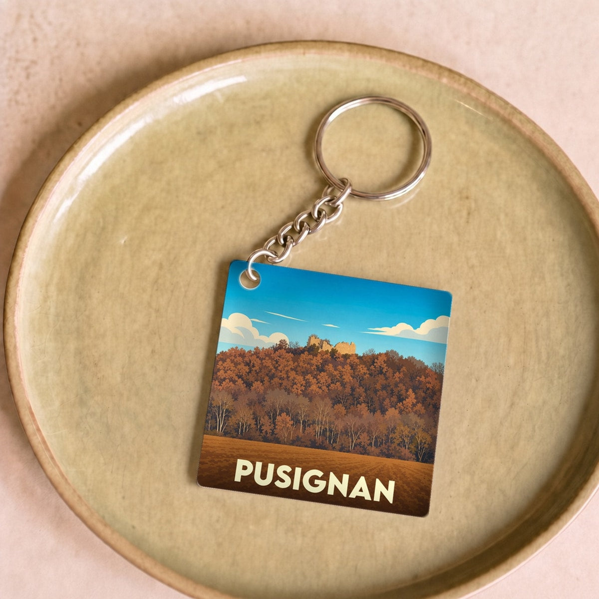 Porte-clés souvenir de la ville de Pusignan avec une illustration stylisée d'un paysage automnal.