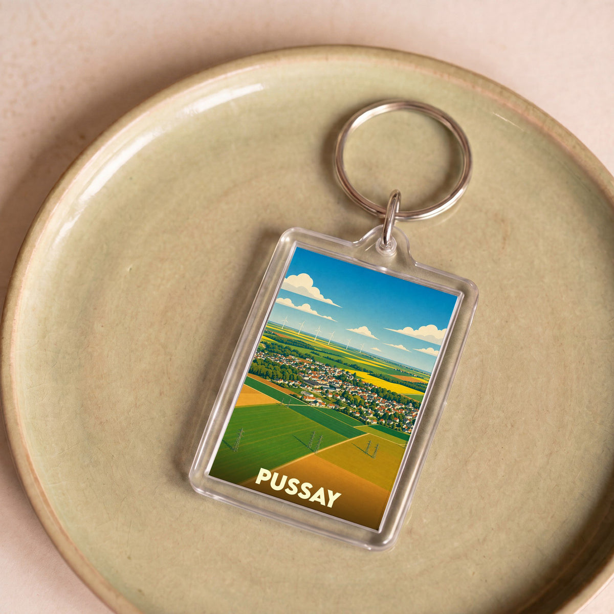 Porte-clés souvenir de la ville de Pussay avec une illustration stylisée de ses paysages.