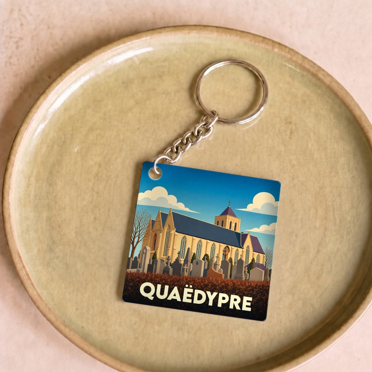 Porte-clés souvenir de la ville de Quaëdypre avec une illustration stylisée de son église et de son cimetière.