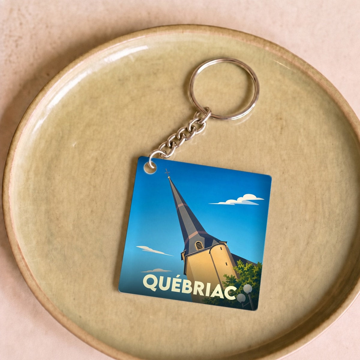 Porte-clés souvenir de la ville de Québriac avec une illustration stylisée de son église.