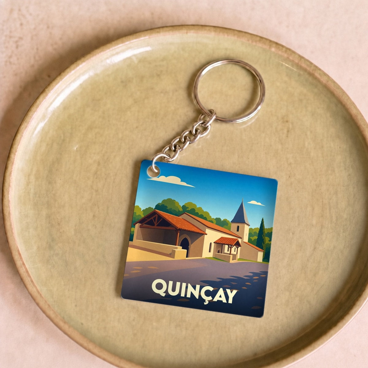 Porte-clés souvenir de la ville de Quinçay avec une illustration stylisée de son église et de ses bâtiments.