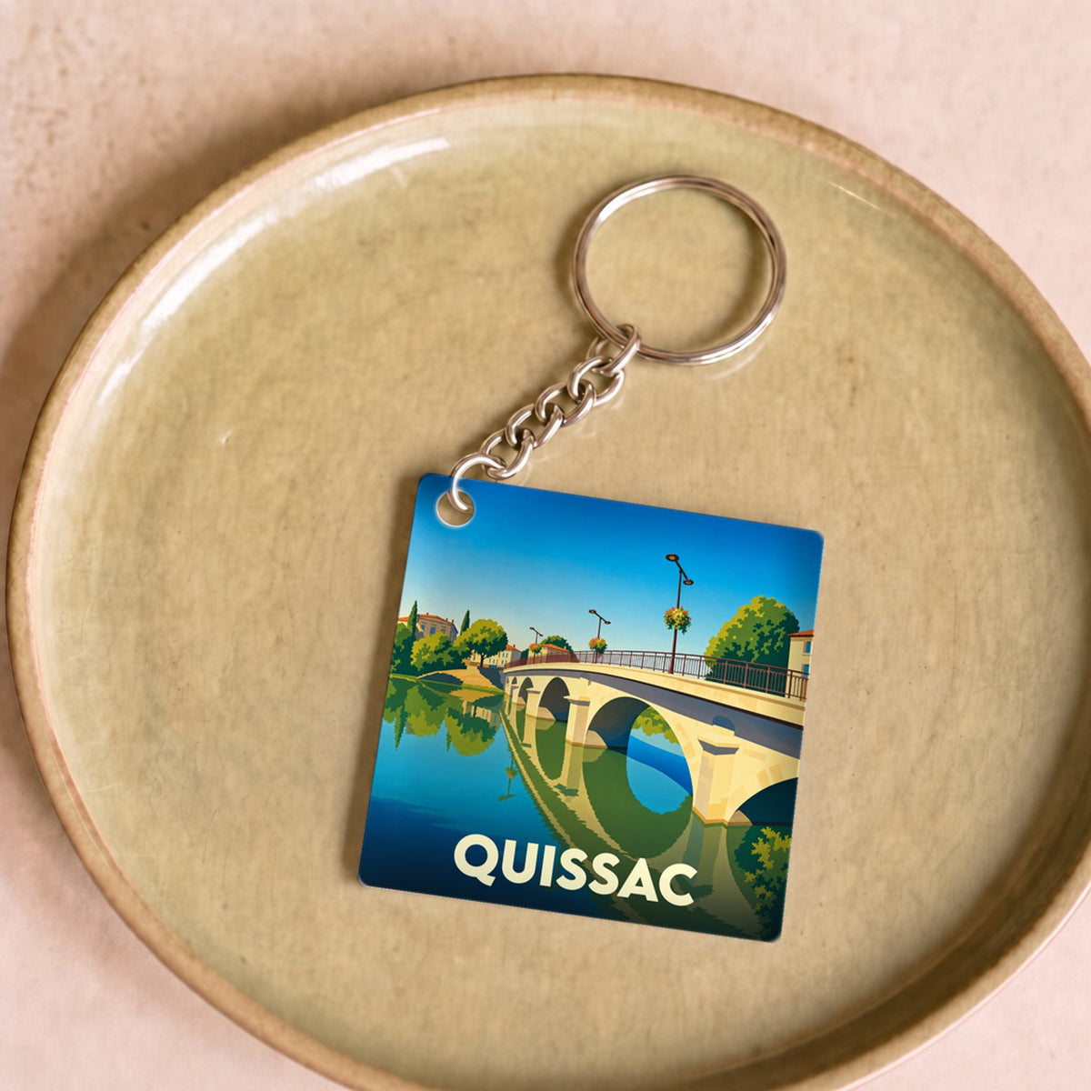 Porte-clés souvenir de la ville de Quissac avec une illustration stylisée de son pont.