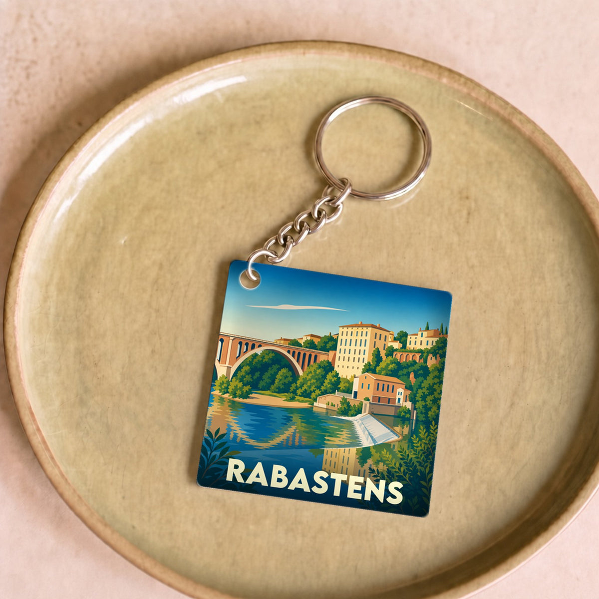 Porte-clés souvenir de la ville de Rabastens avec une illustration stylisée d'un pont et de bâtiments au bord de l'eau.