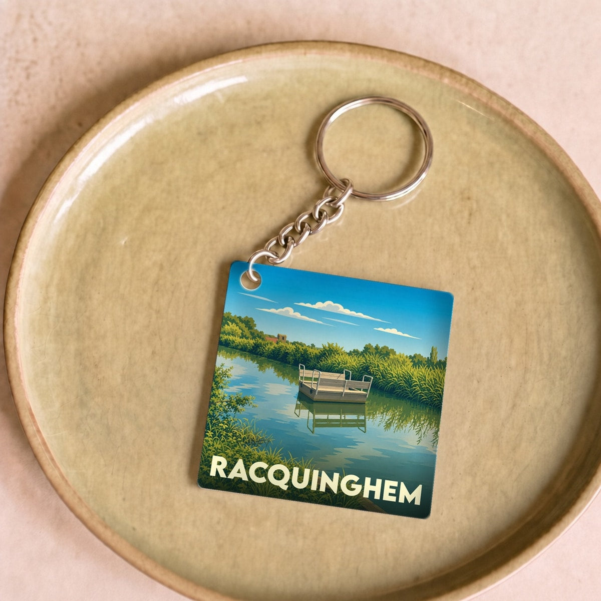 Porte-clés souvenir de la ville de Racquinghem avec une illustration stylisée d'un paysage fluvial.