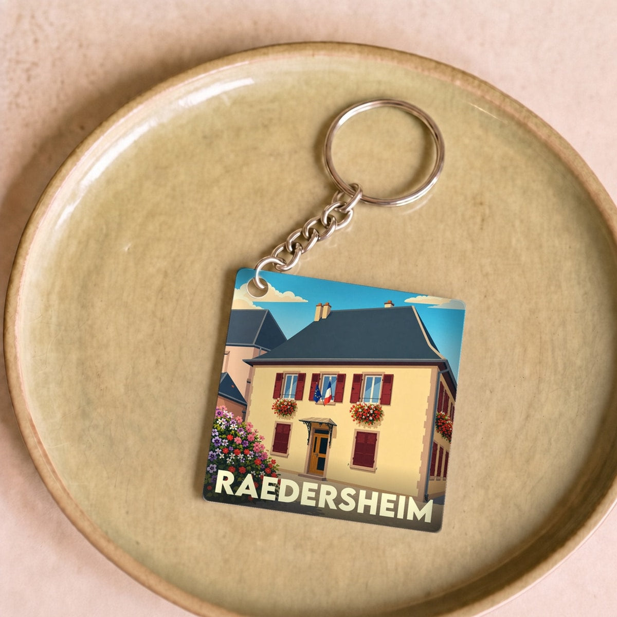 Porte-clés souvenir de la ville de Raedersheim avec une illustration stylisée de sa mairie fleurie.