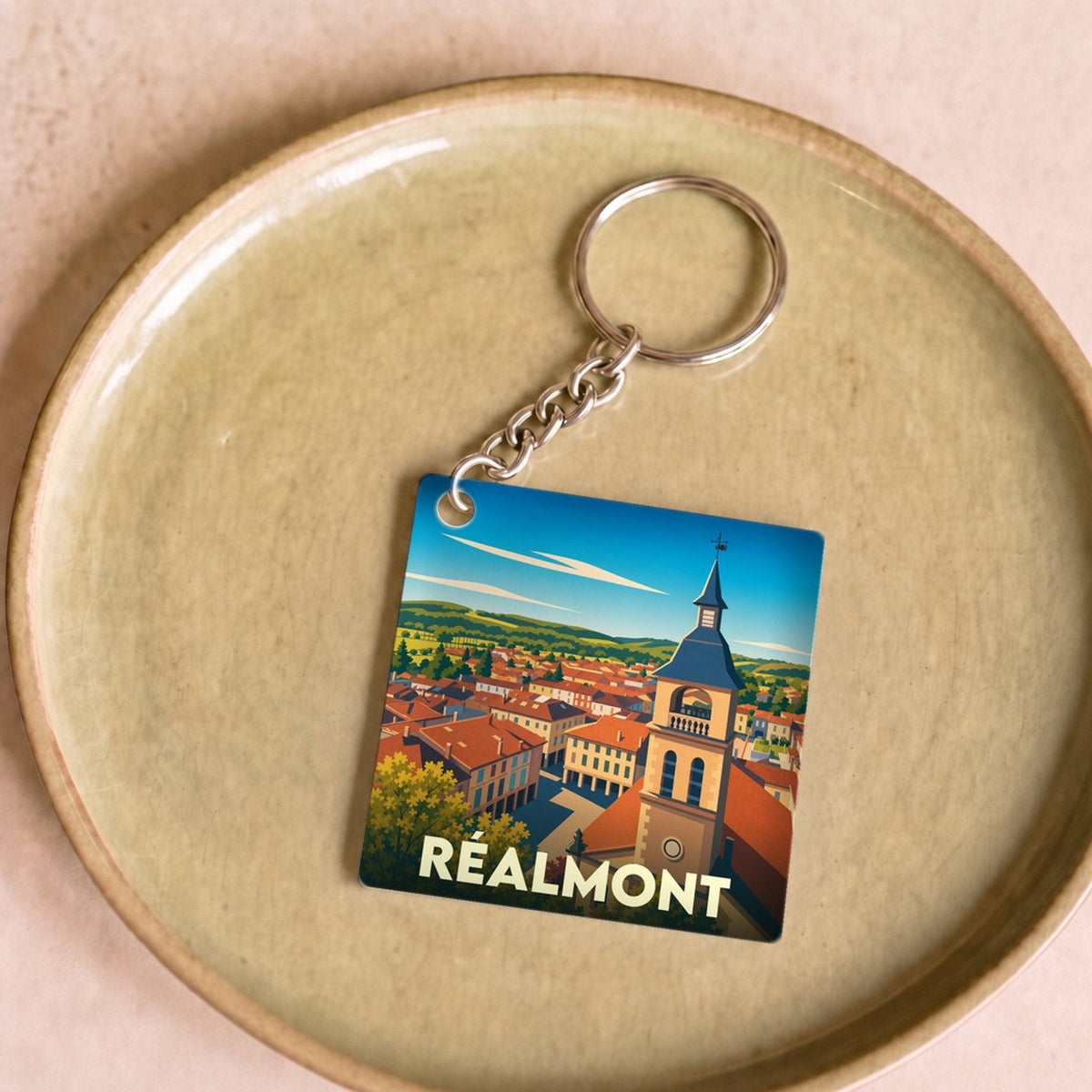Porte-clés souvenir de la ville de Réalmont avec une illustration stylisée de son clocher et de ses toits.