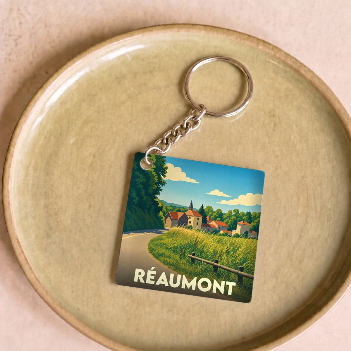 Porte-clés souvenir de la ville de Réaumont avec une illustration champêtre stylisée.