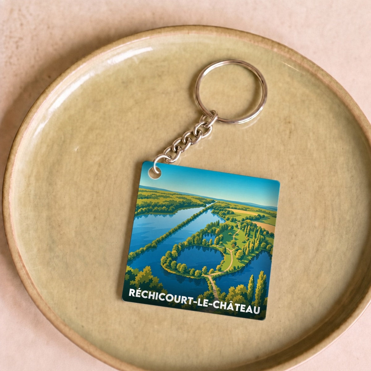 Porte-clés souvenir de la ville de Réchicourt-le-Château avec une illustration stylisée d'un paysage aérien.