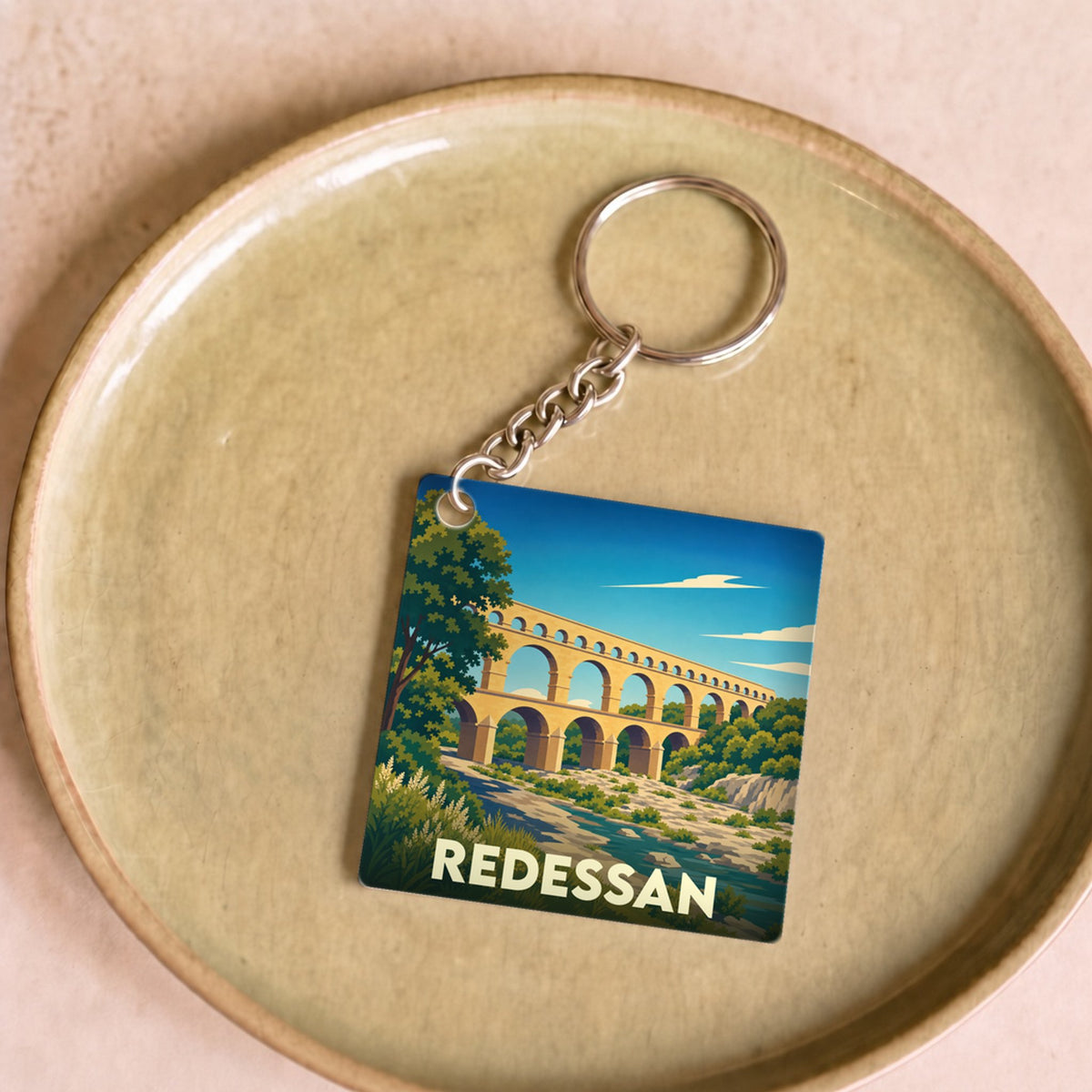 Porte-clés souvenir de la ville de Redessan illustré par un dessin stylisé du Pont du Gard.