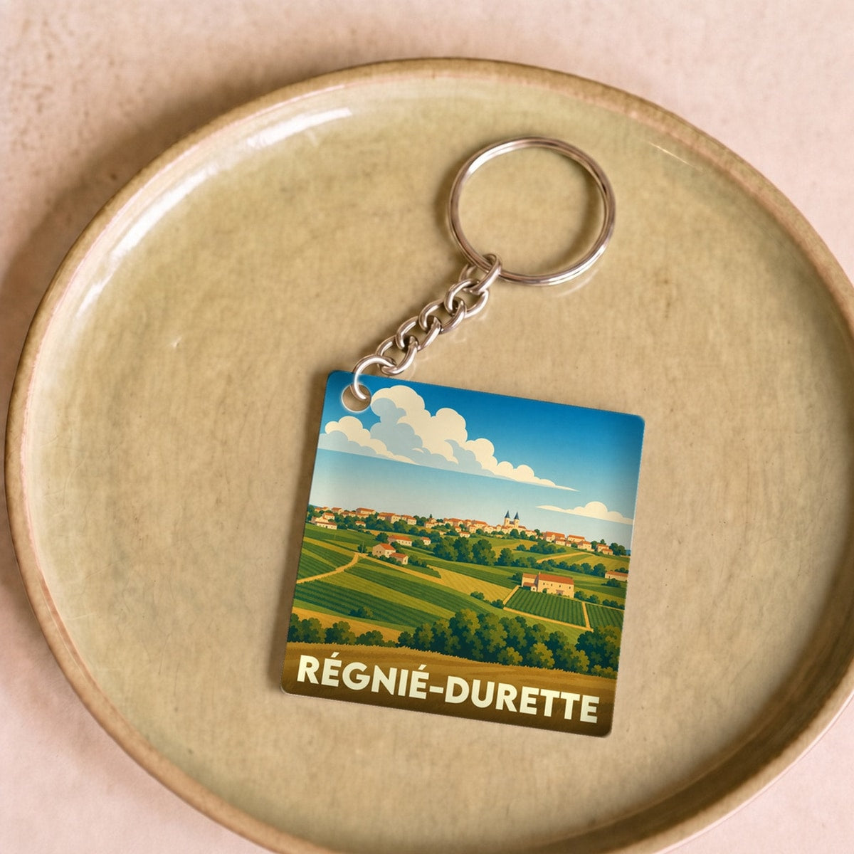 Porte-clés souvenir de la ville de Régnié-Durette avec une illustration stylisée de paysages de vignes.