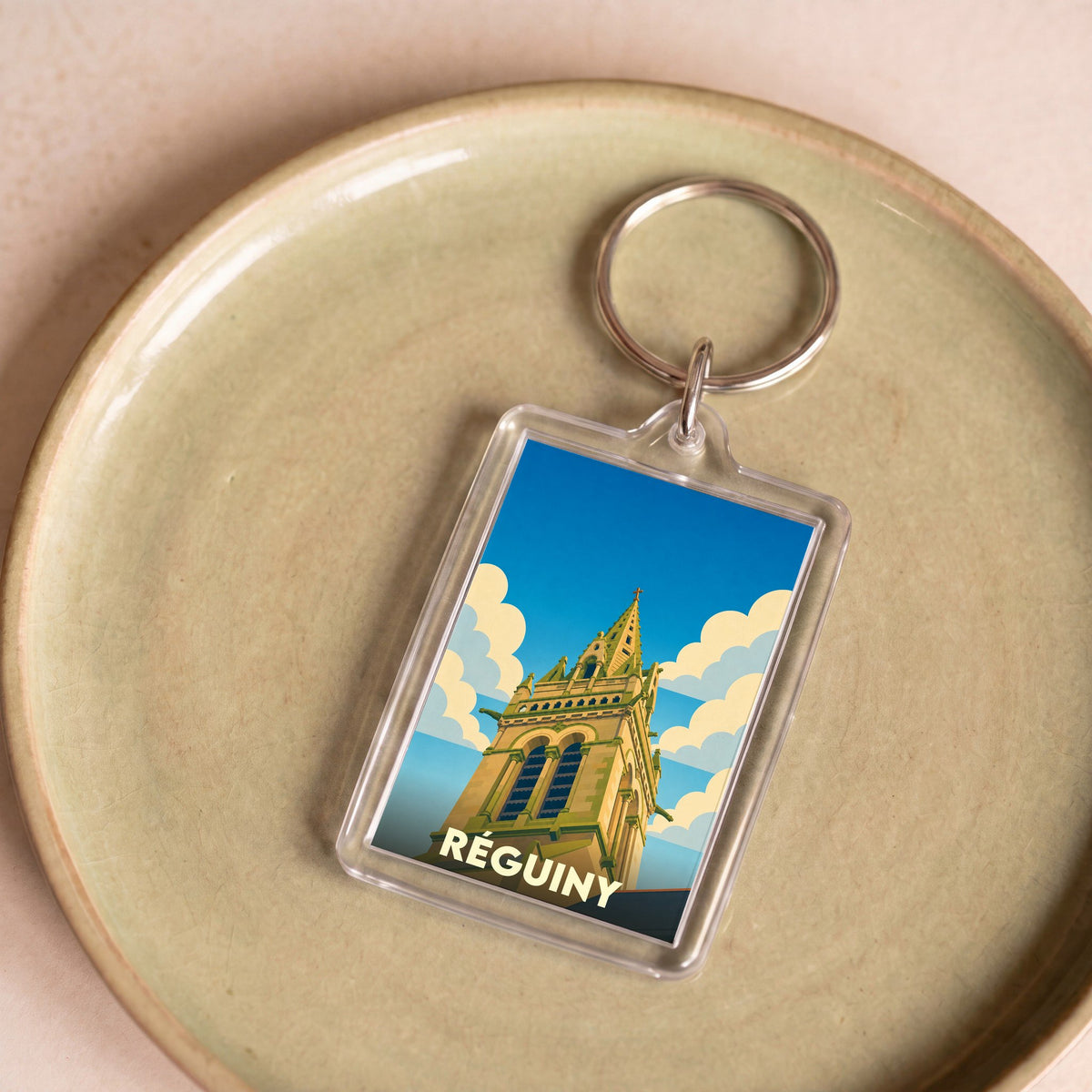 Porte-clés souvenir de la ville de Réguiny avec une illustration stylisée d'un clocher.